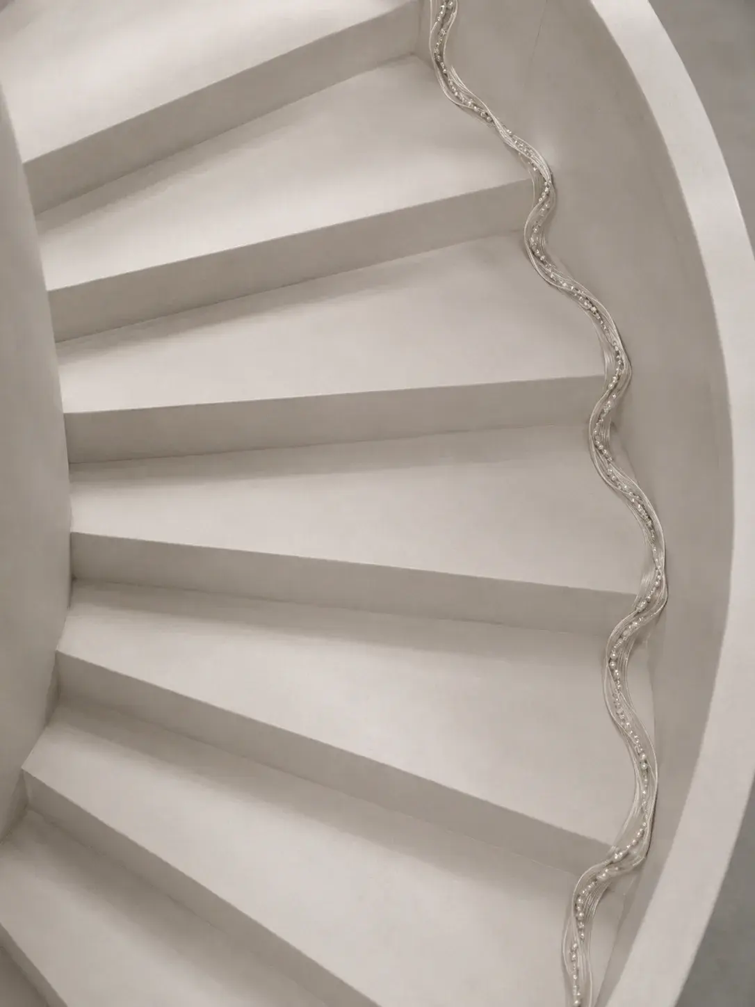 Escalier hélicoïdal blanc vu du dessus avec un fil de perles courant en spirale le long de la rampe