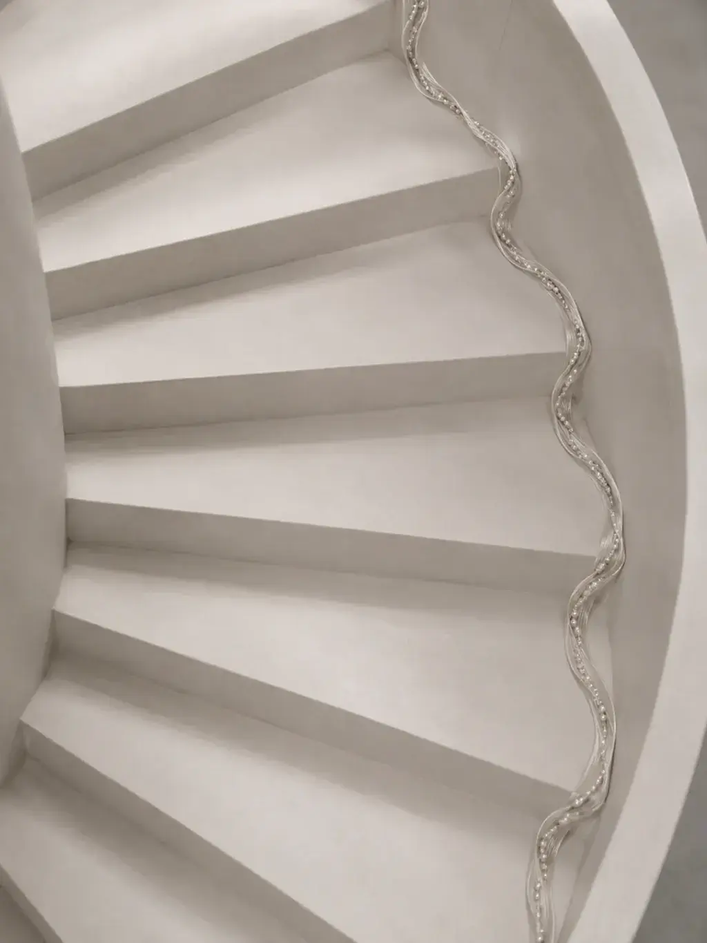 Escalier hélicoïdal blanc vu du dessus avec un fil de perles courant en spirale le long de la rampe