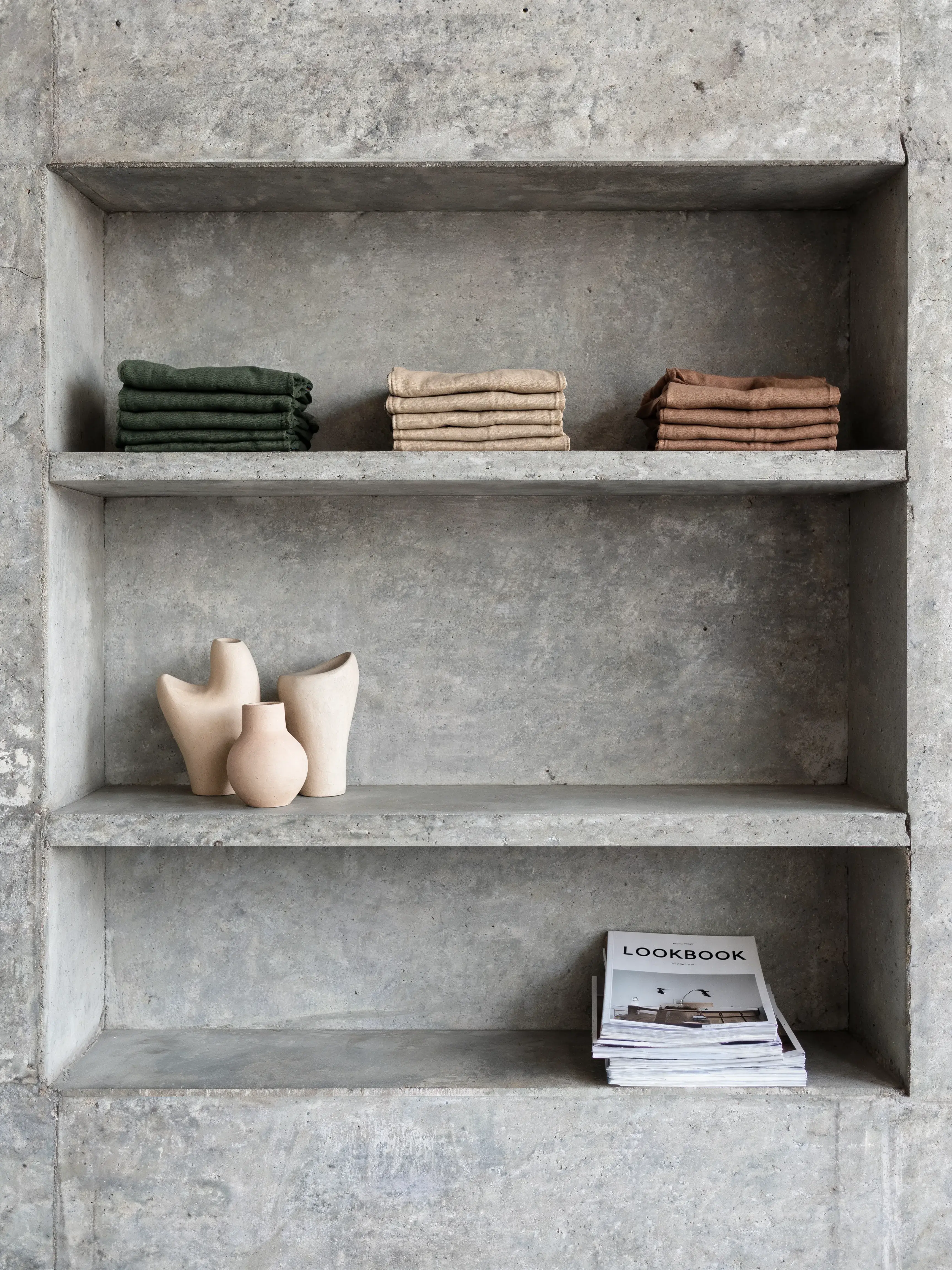 Étagères béton – vêtements pliés colorés, vases céramique, catalogue de collection