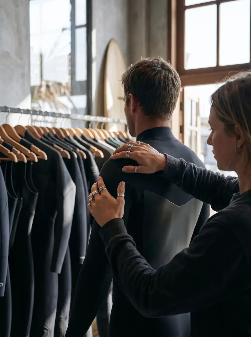 Femme ajustant une combinaison de surf dans le dos d'un homme – boutique surf avec portant