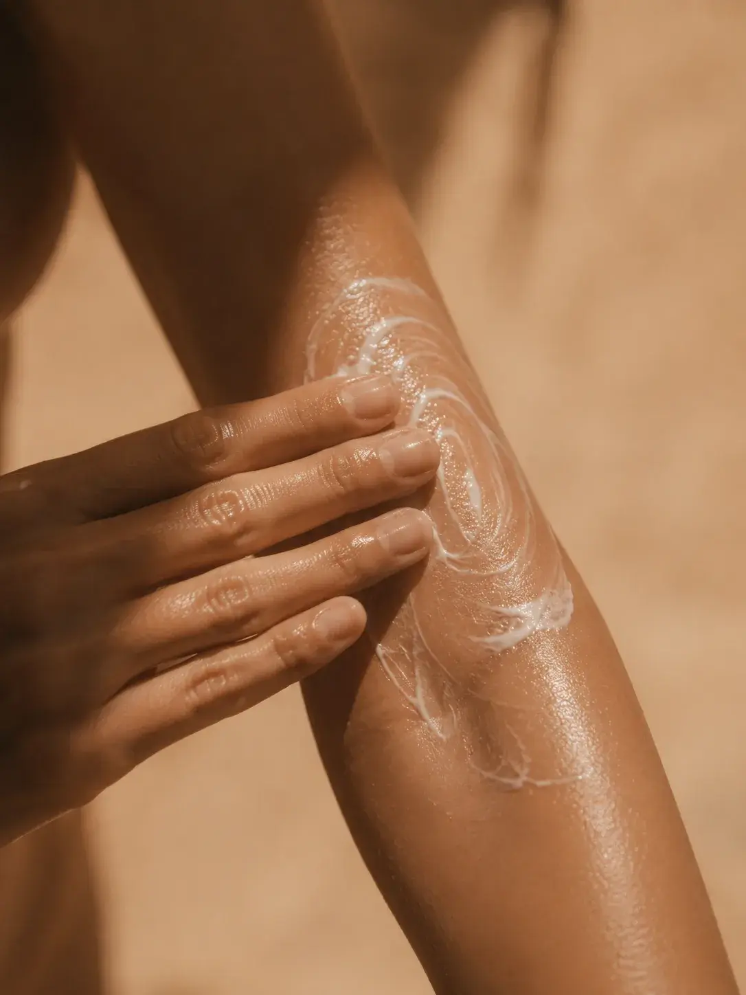 Femme appliquant crème en spirale sur avant-bras – peau bronzée, fond sable désertique