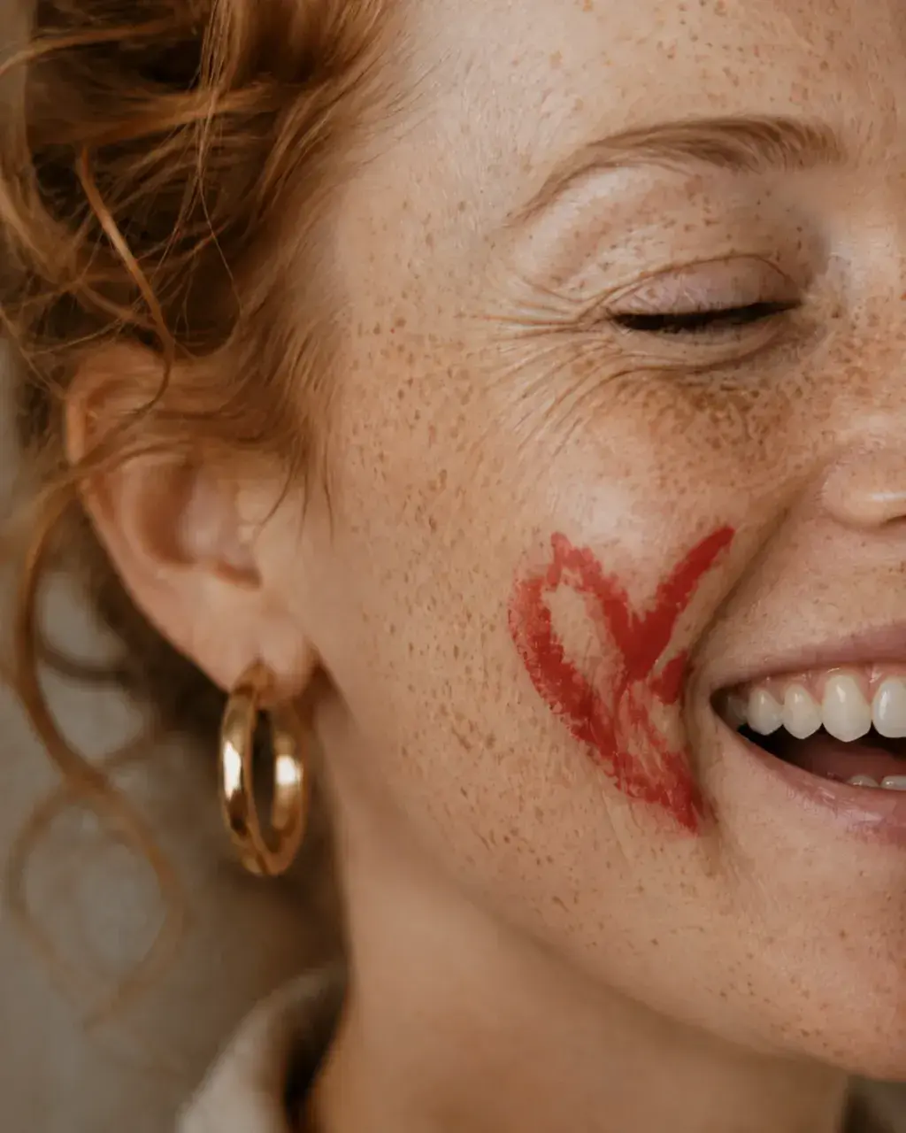 Femme aux taches de rousseur riant avec un cœur dessiné au rouge à lèvres sur la joue