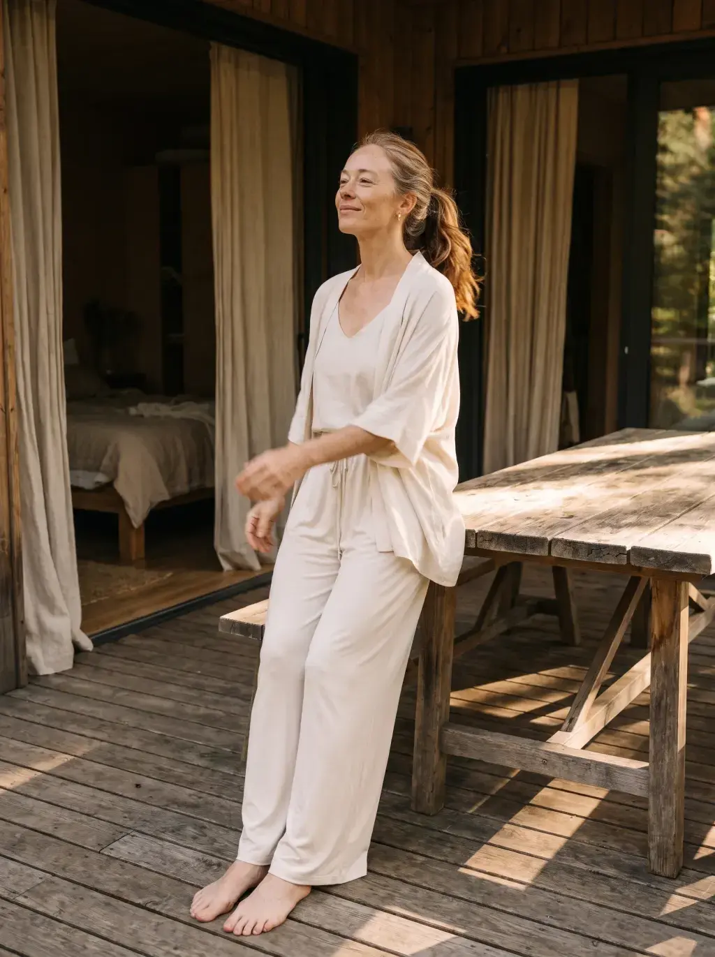 Femme blonde en ensemble lin crème sur une terrasse en bois au soleil