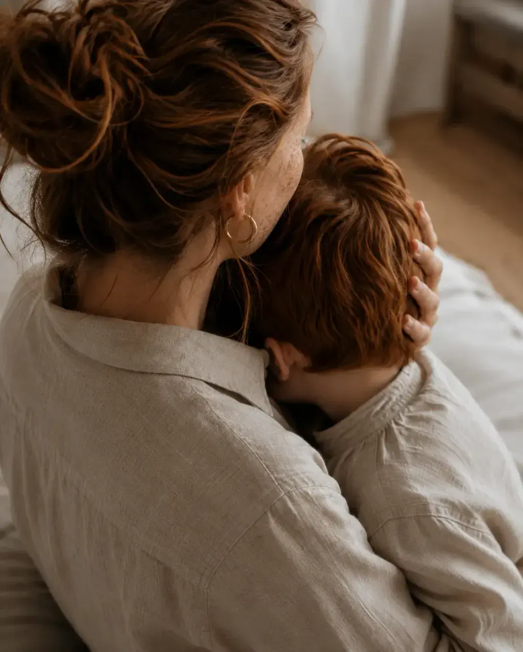 Femme de dos en chemise lin serrant un enfant roux – intérieur chaleureux et lumineux