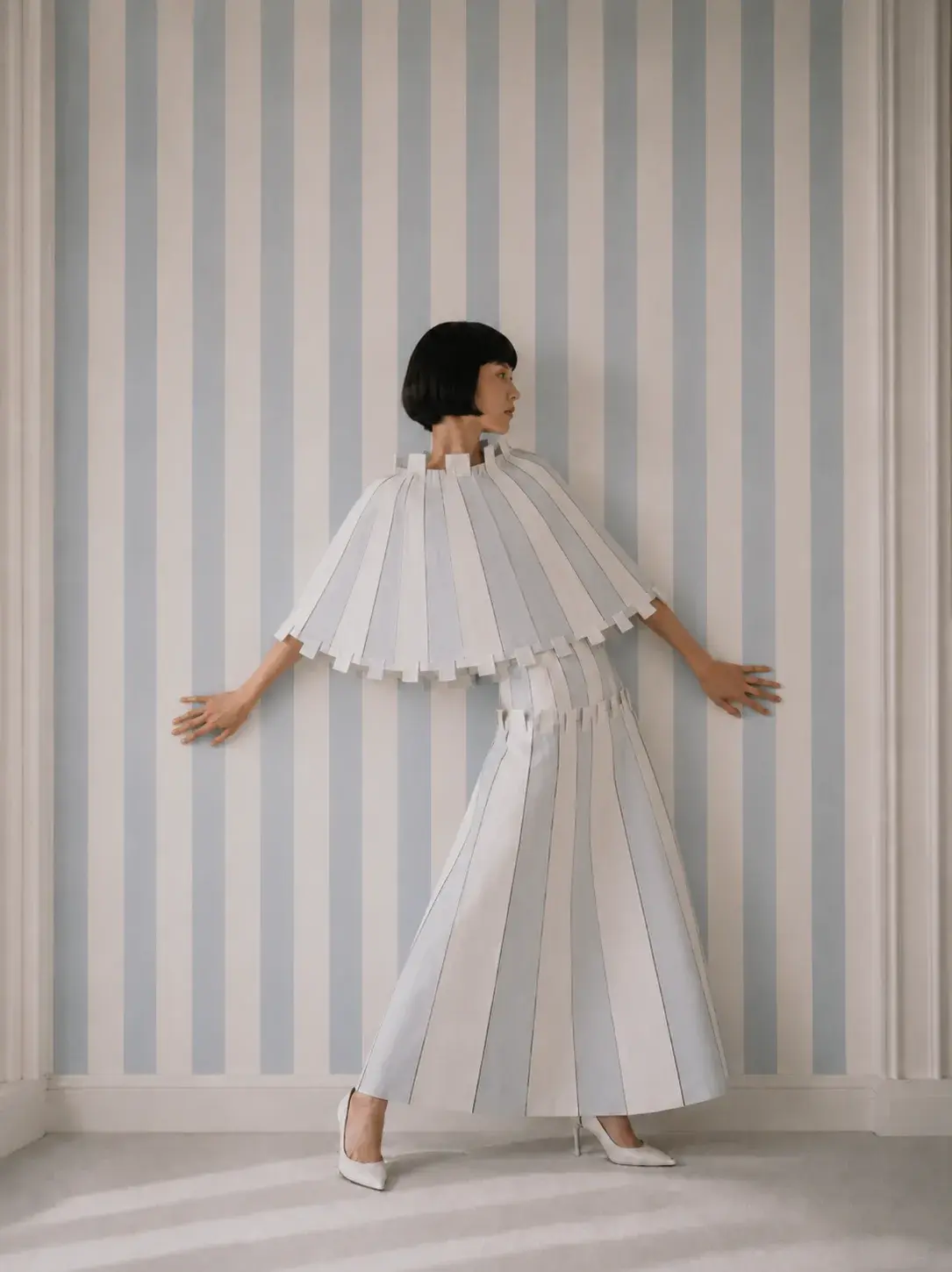 Femme de dos en ensemble origami bras écartés – papier peint rayé bleu et blanc