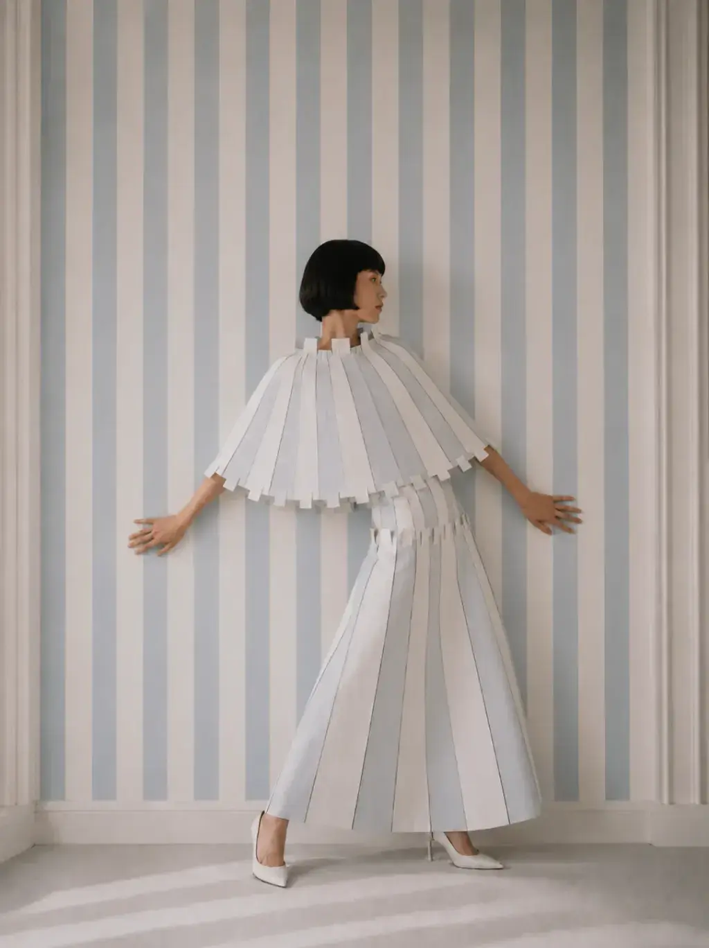 Femme de dos en ensemble origami bras écartés – papier peint rayé bleu et blanc