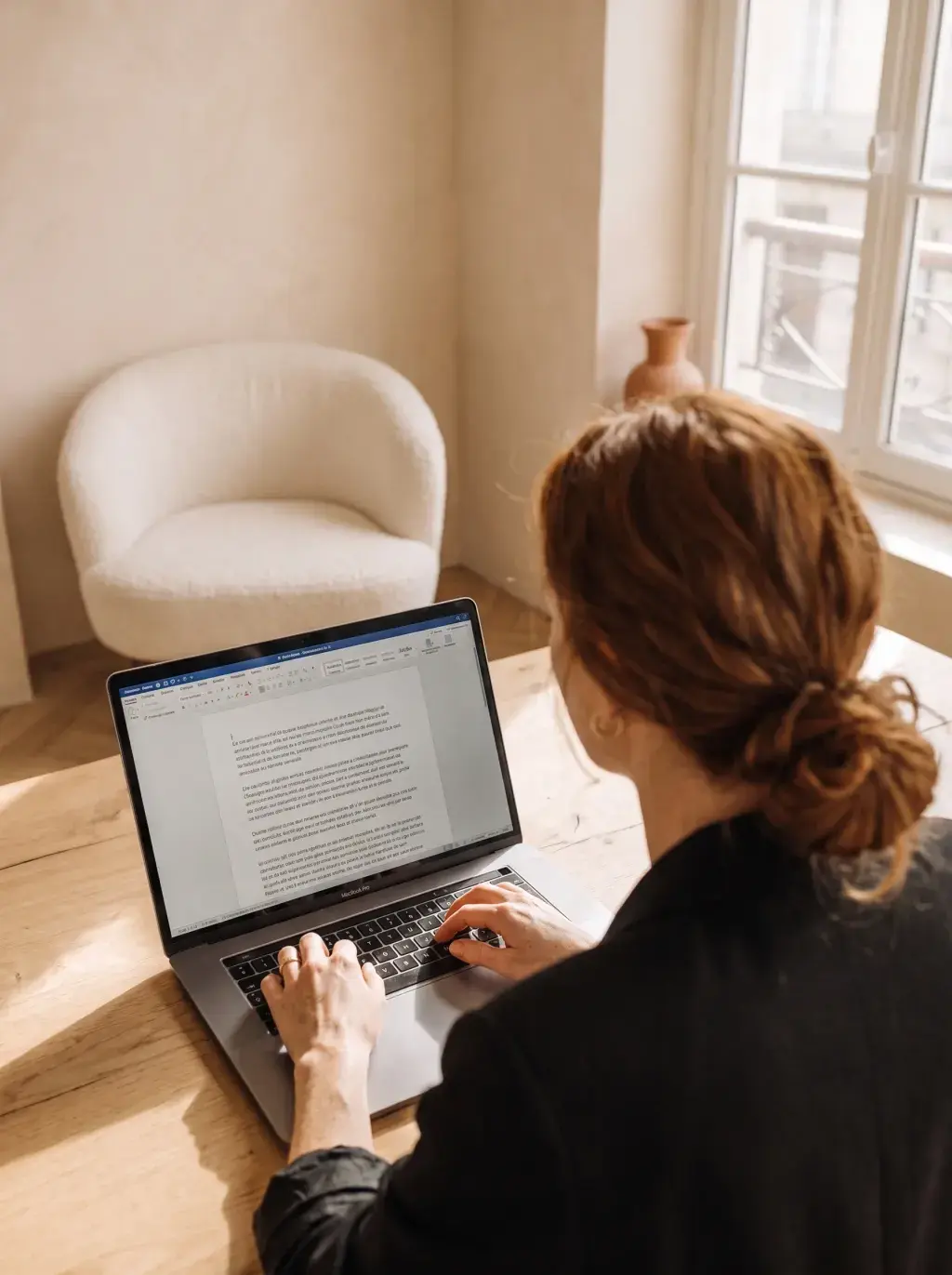 Femme de dos travaillant sur un document Word depuis son laptop