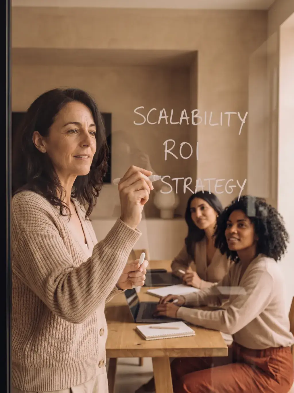 Femme écrivant Scalability ROI Strategy sur une vitre devant son équipe dans un bureau