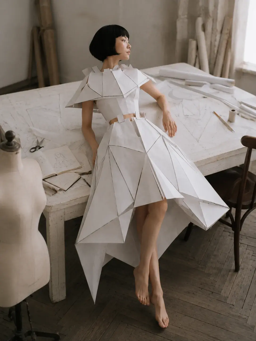 Femme en robe origami dans atelier de couture – mannequin, patrons et table de travail