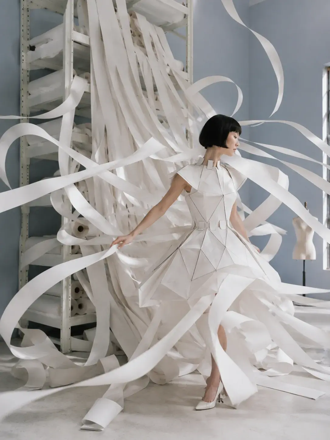 Femme en robe origami entourée de rubans de papier déroulants – atelier industriel bleu