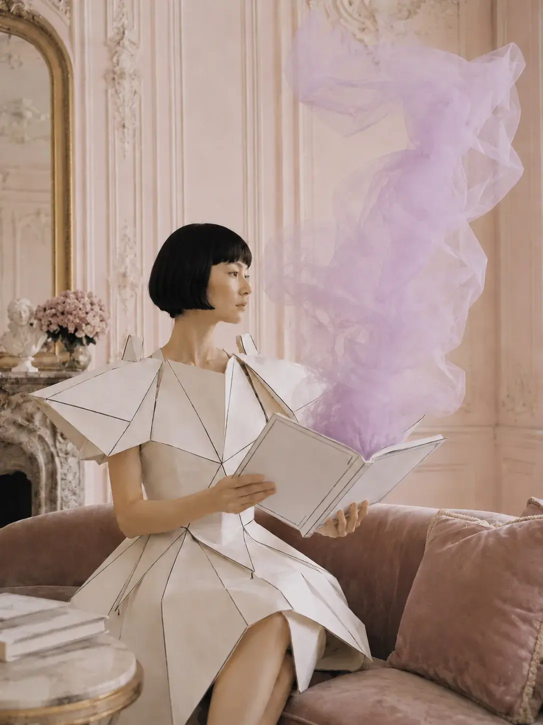 Femme en robe origami lisant dans salon baroque rose – nuage de tulle violet s'échappant du livre