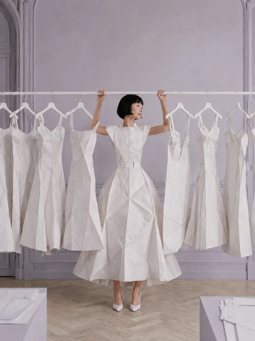 Femme en robe origami regardant de côté devant portant de robes – salon haussmannien gris
