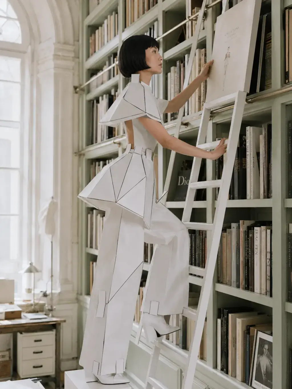 Femme en tenue origami montant une échelle dans bibliothèque haussmannienne