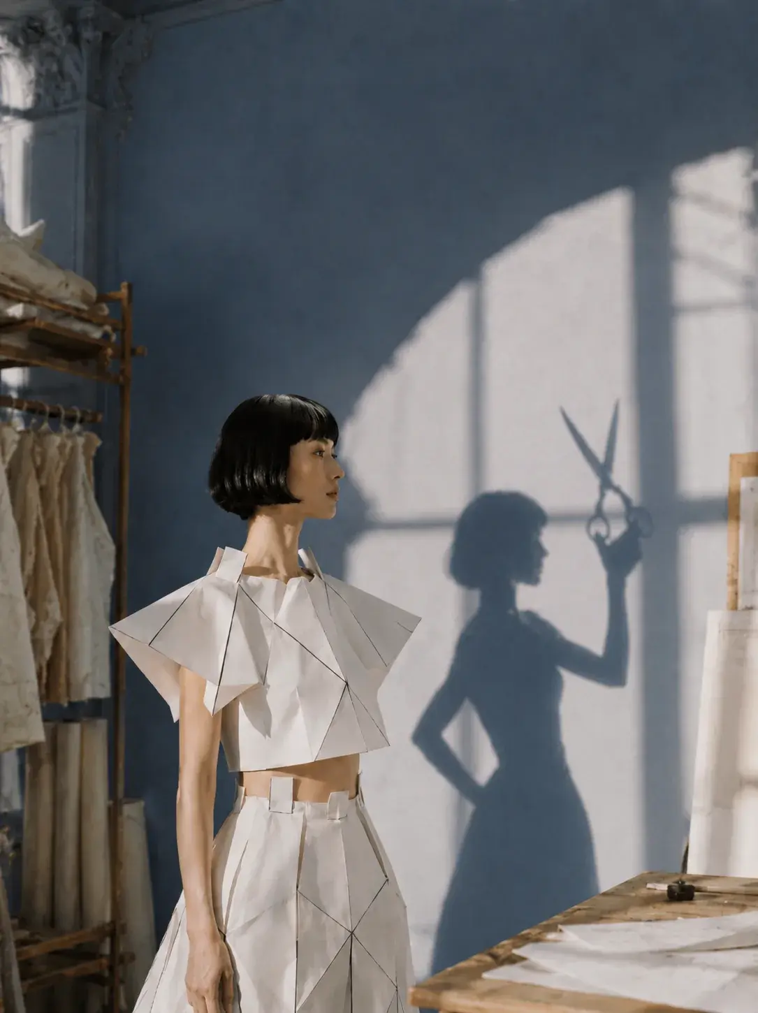 Femme en top origami avec ombre de ciseaux géants – atelier couture mur bleu