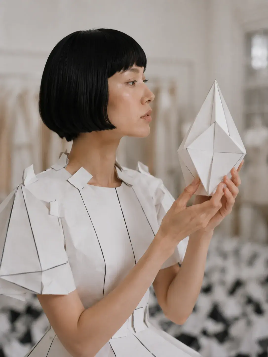 Femme en top origami tenant une sculpture géométrique en papier – atelier couture et pyramides