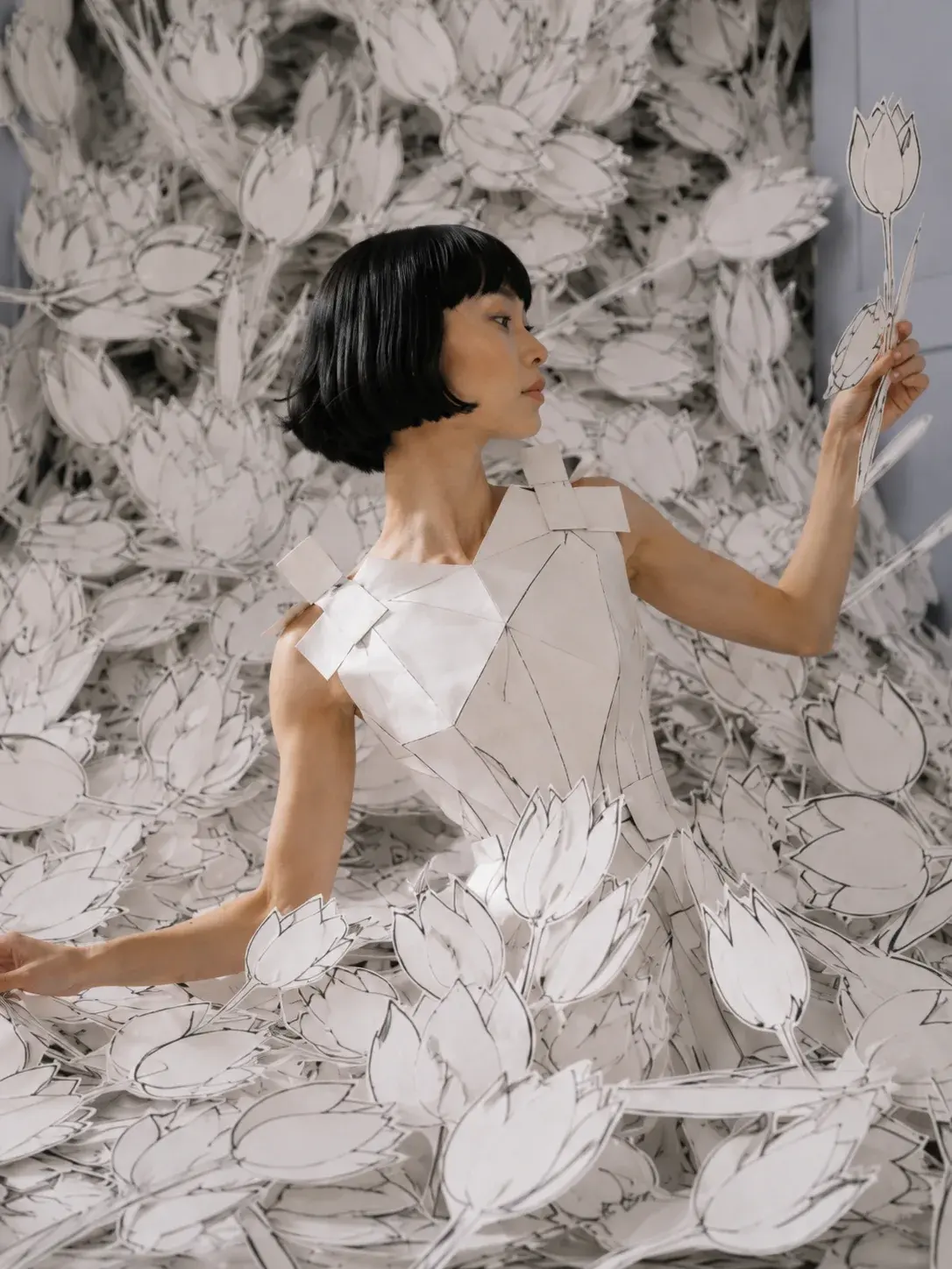 Femme en top origami tenant une tulipe en papier – entourée de fleurs découpées en salon haussmannien