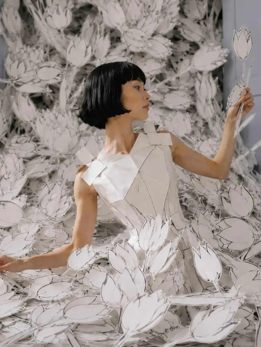 Femme en top origami tenant une tulipe en papier – entourée de fleurs découpées en salon haussmannien