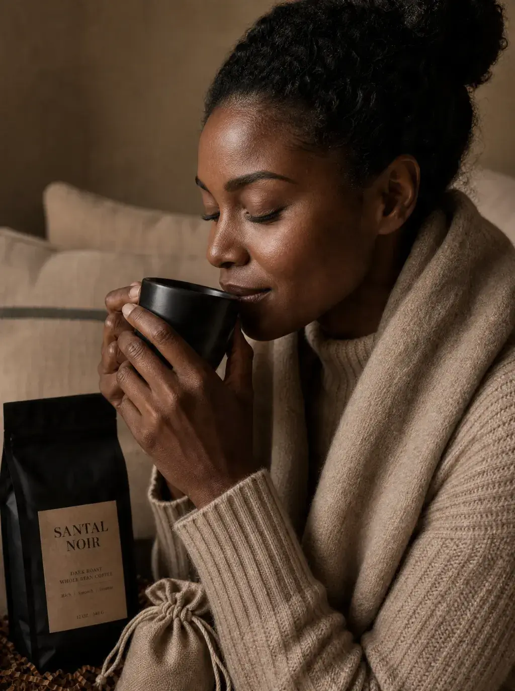 Femme humant café dans mug noir – pull beige, canapé, sachet café artisanal