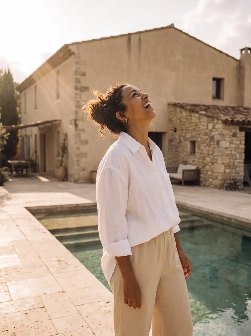 Femme noire en lin blanc et beige au bord d'une piscine de bastide