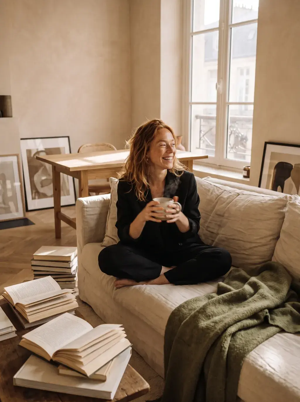 Femme rousse détendue sur un canapé avec thé et livres éparpillés