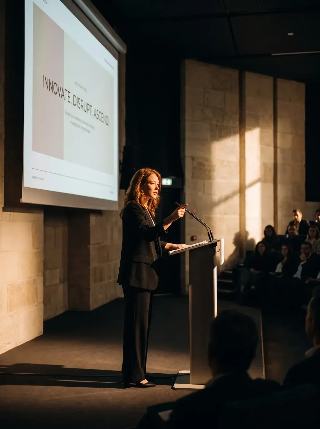 Femme rousse donnant une conférence sur scène devant un grand amphi