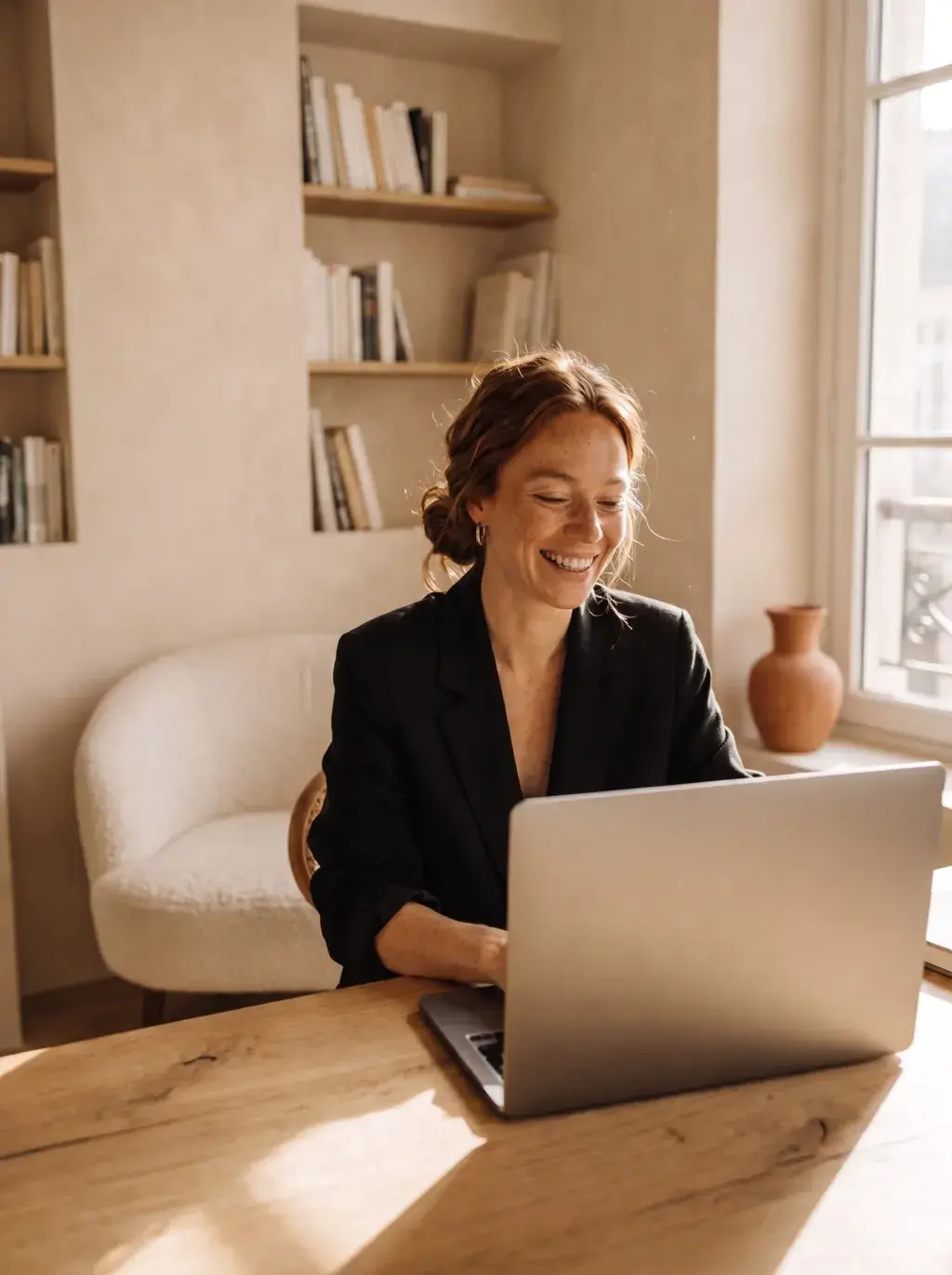 Femme rousse en blazer noir souriante devant son ordinateur