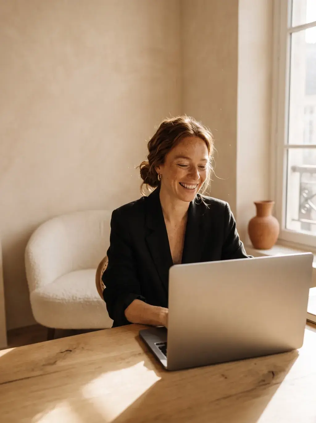 Femme rousse en blazer noir travaillant sur laptop dans un intérieur lumineux