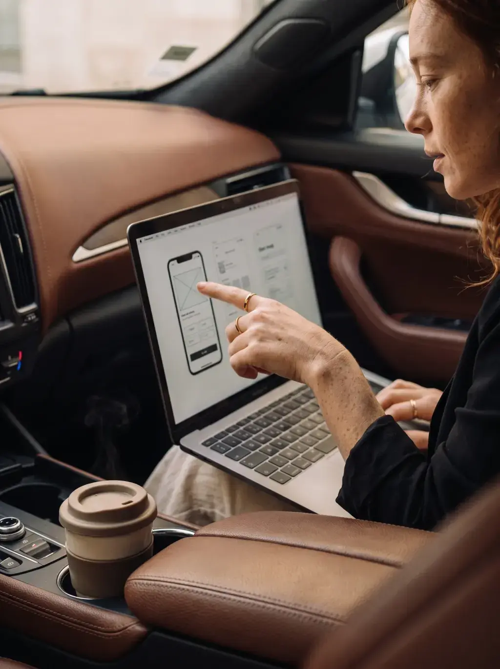 Femme rousse pointant des wireframes sur son laptop dans un véhicule de luxe