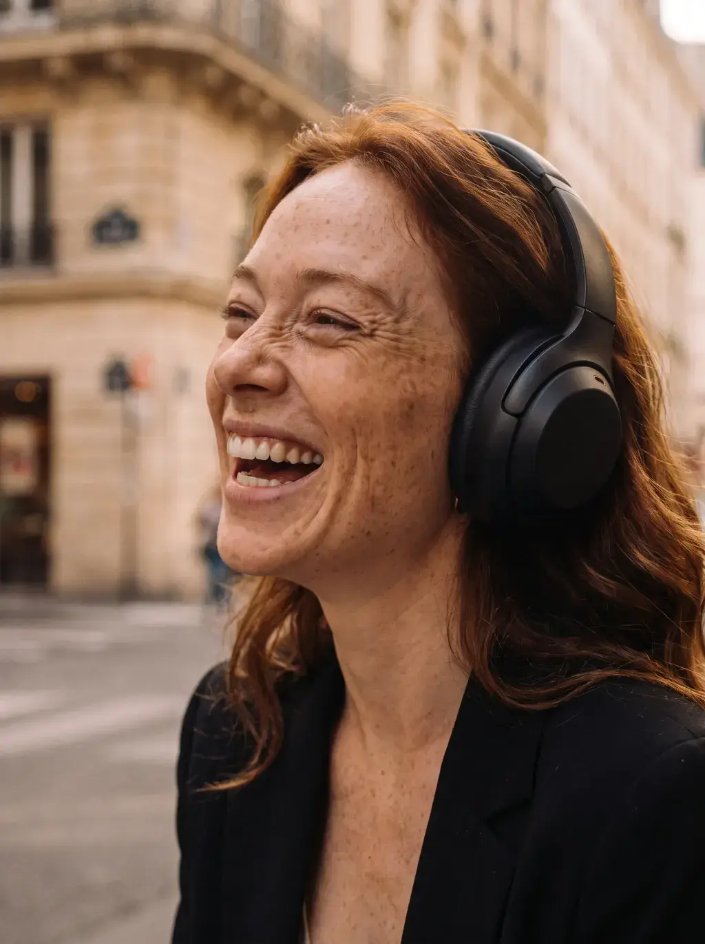Femme rousse riant avec un casque audio dans une rue parisienne haussmannienne
