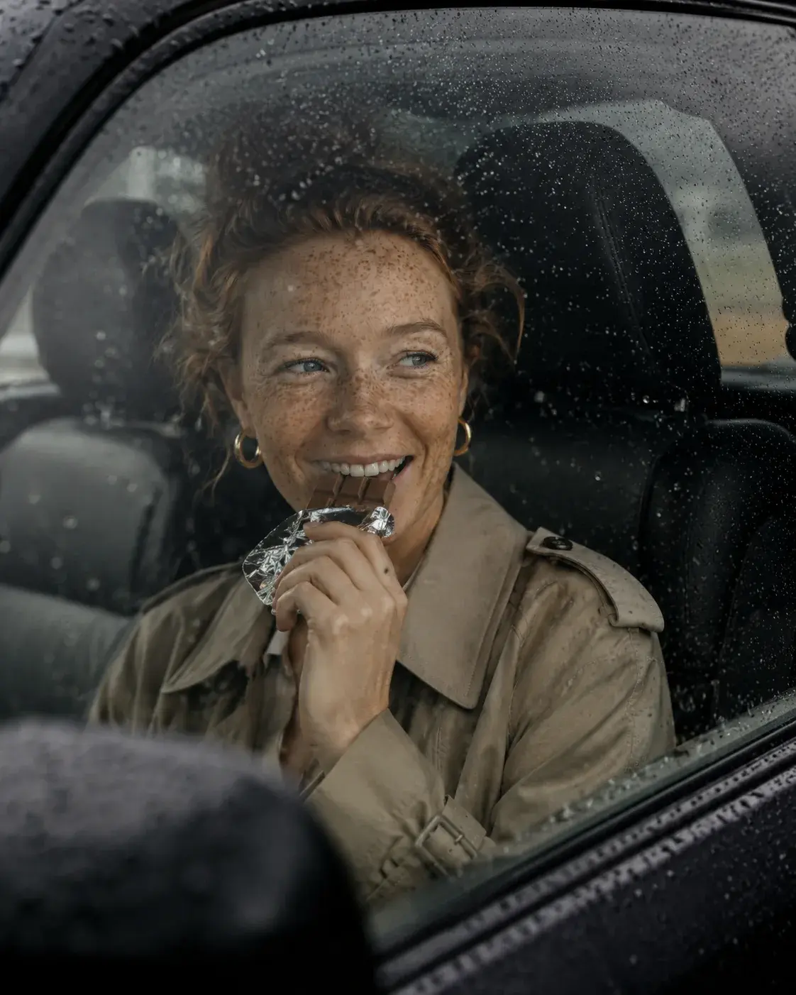 Femme rousse souriante dans sa voiture sous la pluie