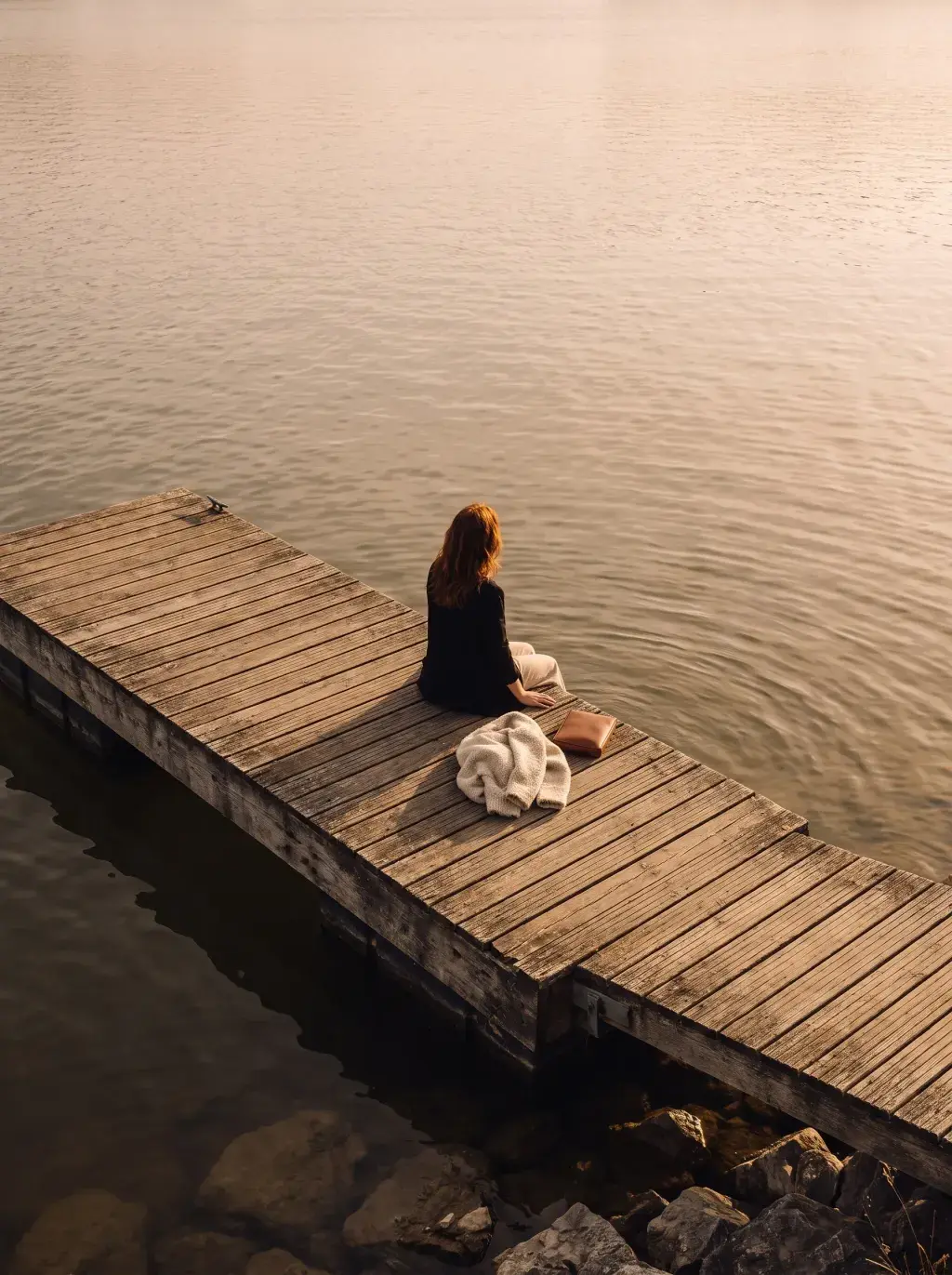 Femme rousse vue de dos méditant sur un ponton en bois au bord d'un lac au coucher du soleil