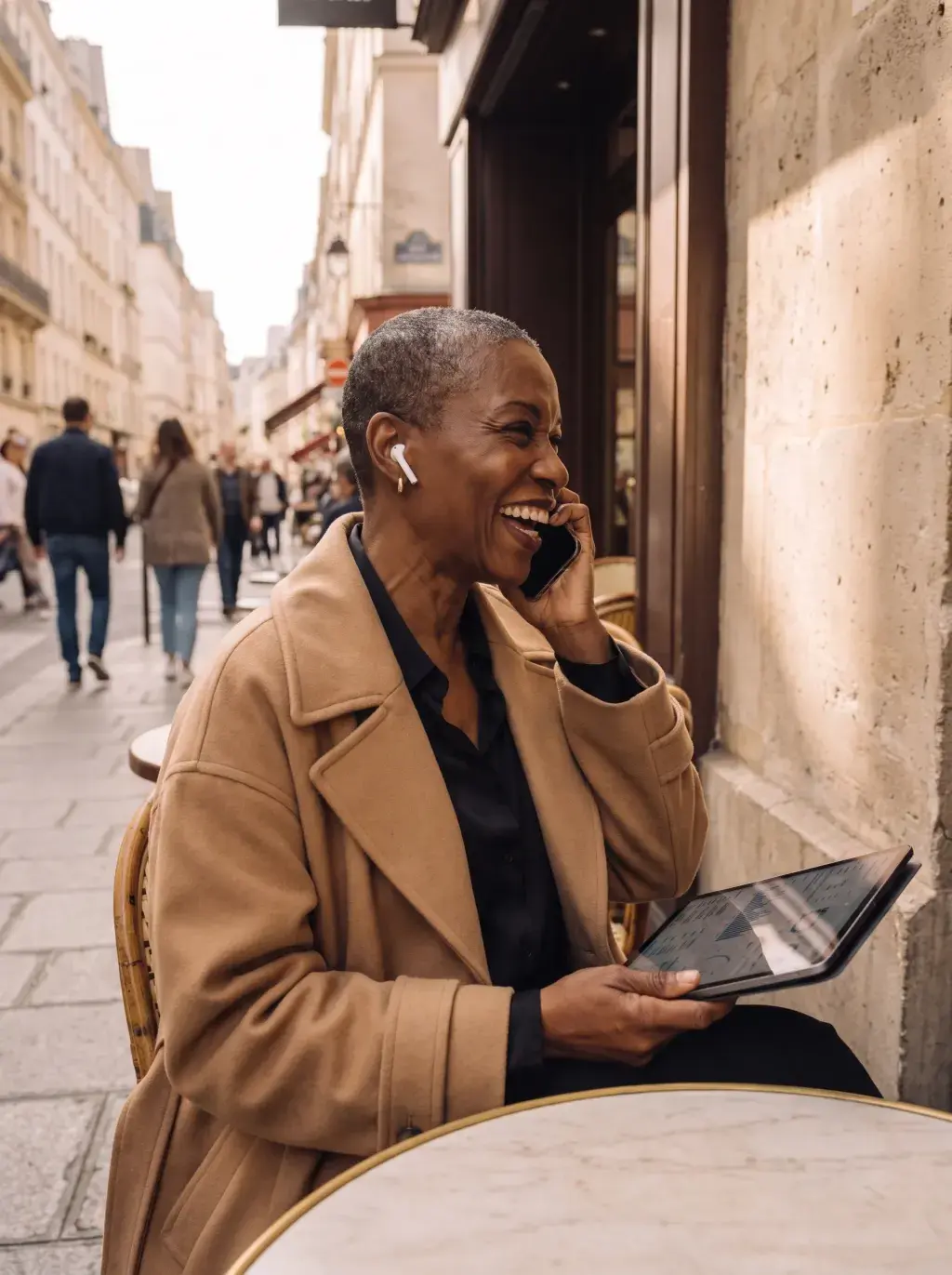 Femme senior noire au téléphone en terrasse parisienne avec tablette