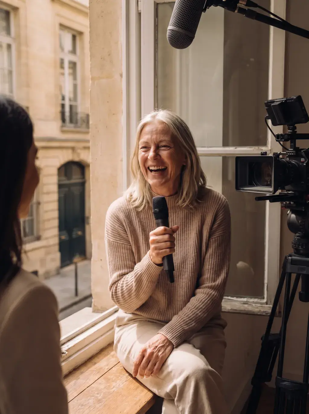 Femme senior riant avec un micro lors d'un tournage interview dans un bureau parisien