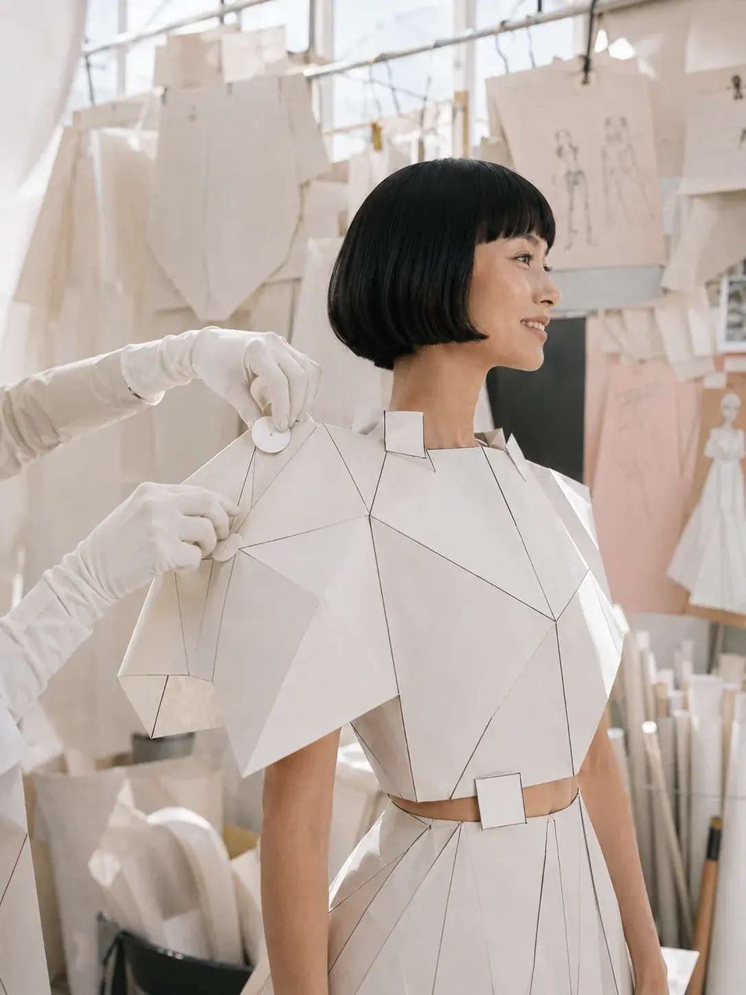 Femme souriante en top origami recevant un élément – atelier couture avec esquisses