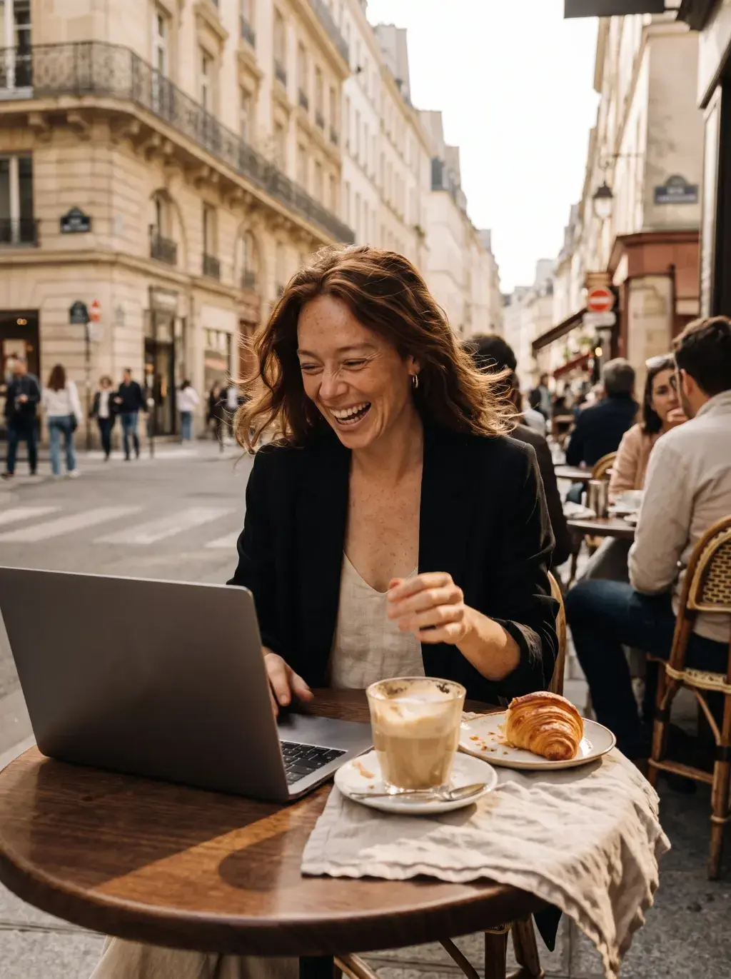 Femme travaillant sur son laptop en terrasse de café parisien en riant