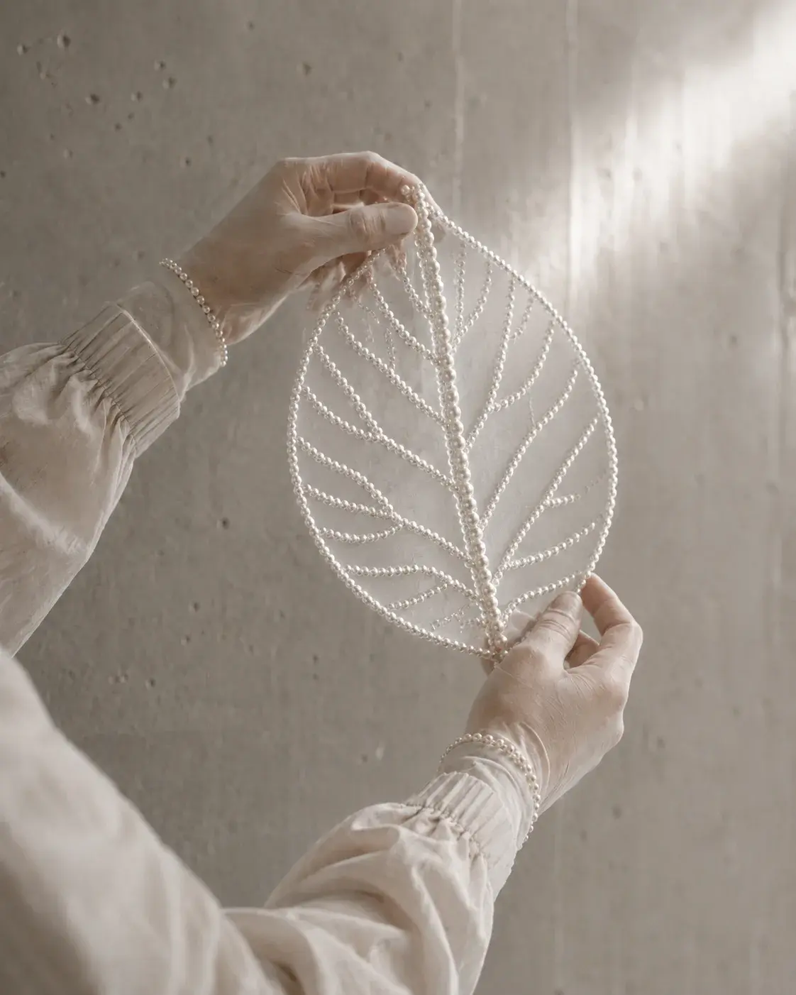 Feuille squelette en perles tenue à deux mains, sculpture végétale nacrée