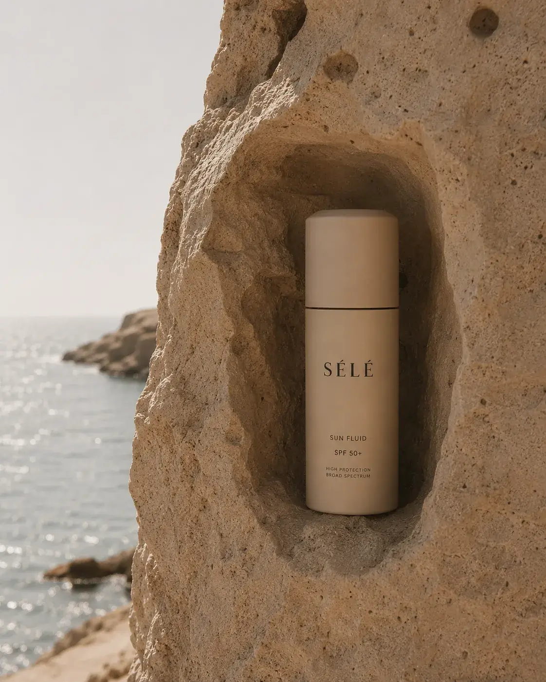 Flacon crème solaire beige dans niche de rocher côtier – mer bleue, ciel, falaises