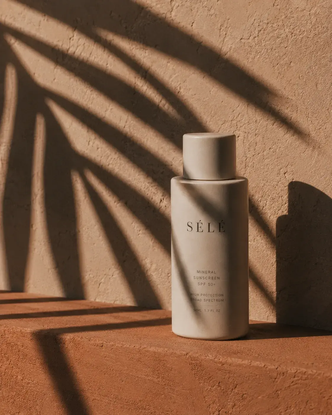 Flacon crème solaire beige mat sur brique terre cuite – ombre de palmier, lumière dramatique
