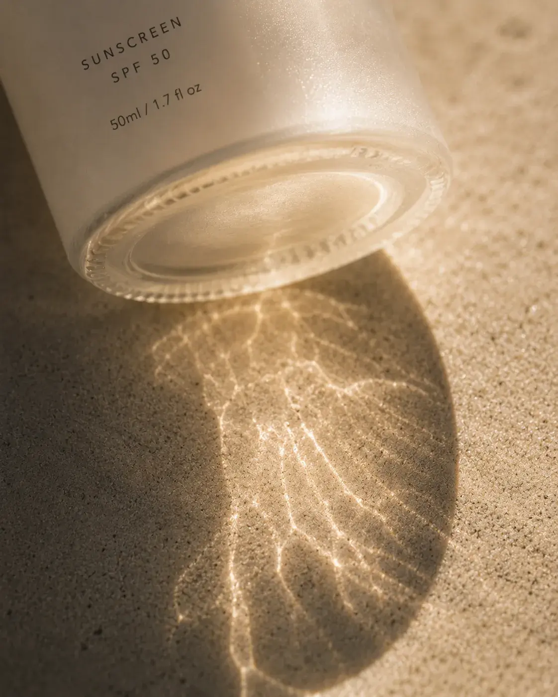 Flacon de crème solaire couché sur sable humide – reflets lumineux aquatiques en dessous