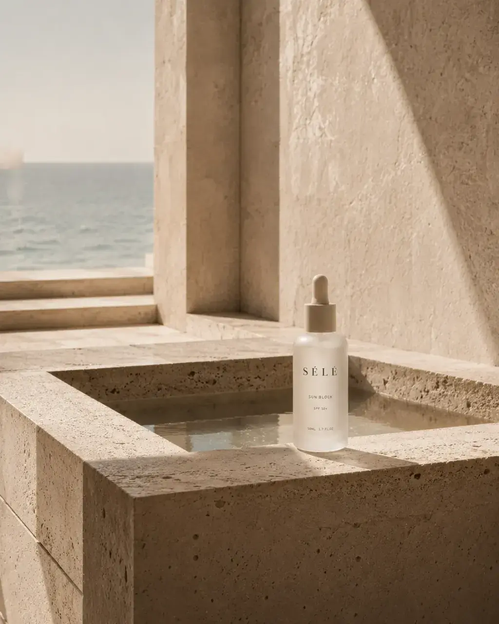 Flacon sérum pipette dans bassin de travertin – architecture côtière luxueuse, mer bleue en fond