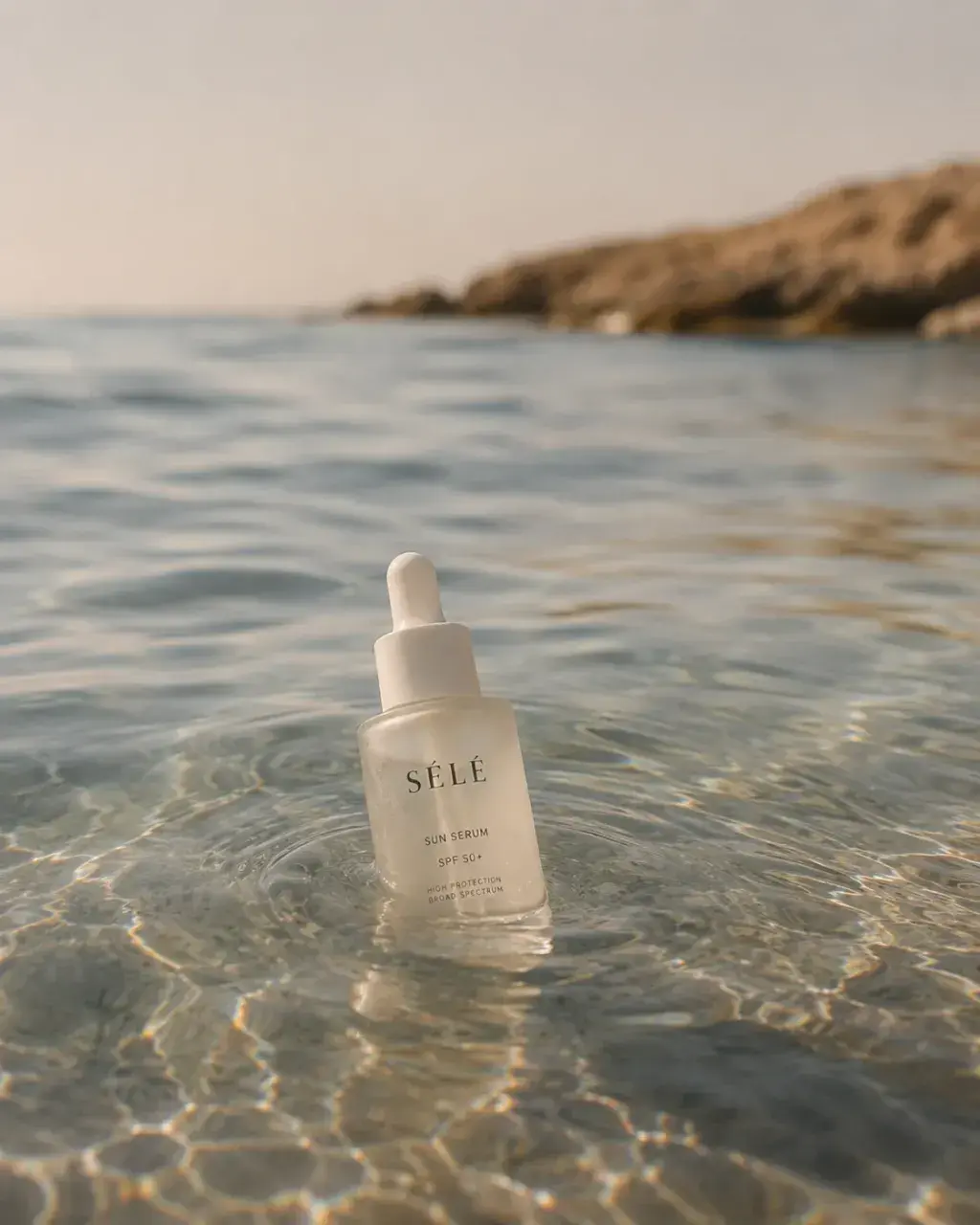 Flacon sérum pipette dans l'eau de mer – reflets, rochers côtiers, coucher de soleil, Méditerranée