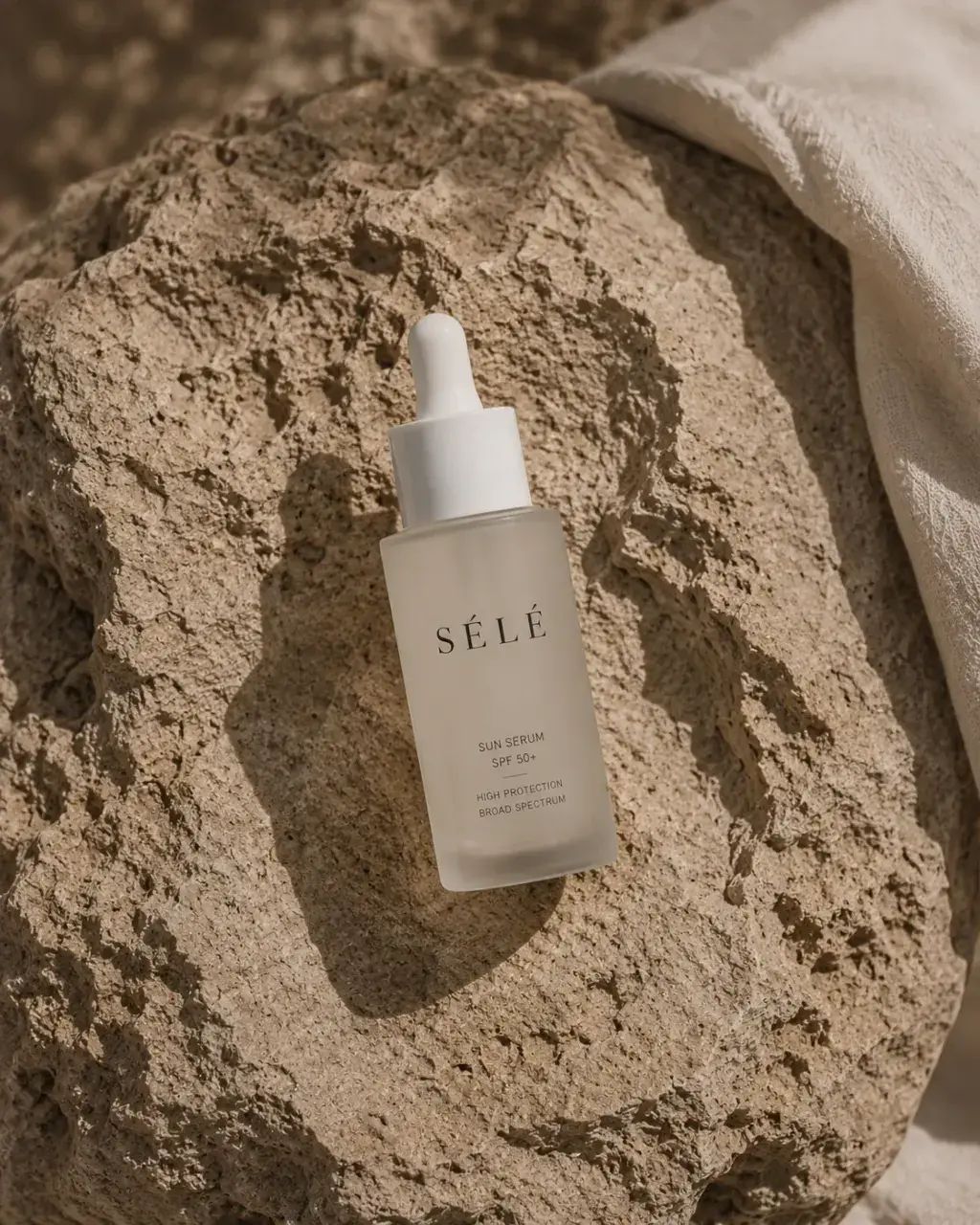 Flacon sérum pipette sur rocher – tissu blanc, lumière sombre dramatique, ambiance minérale