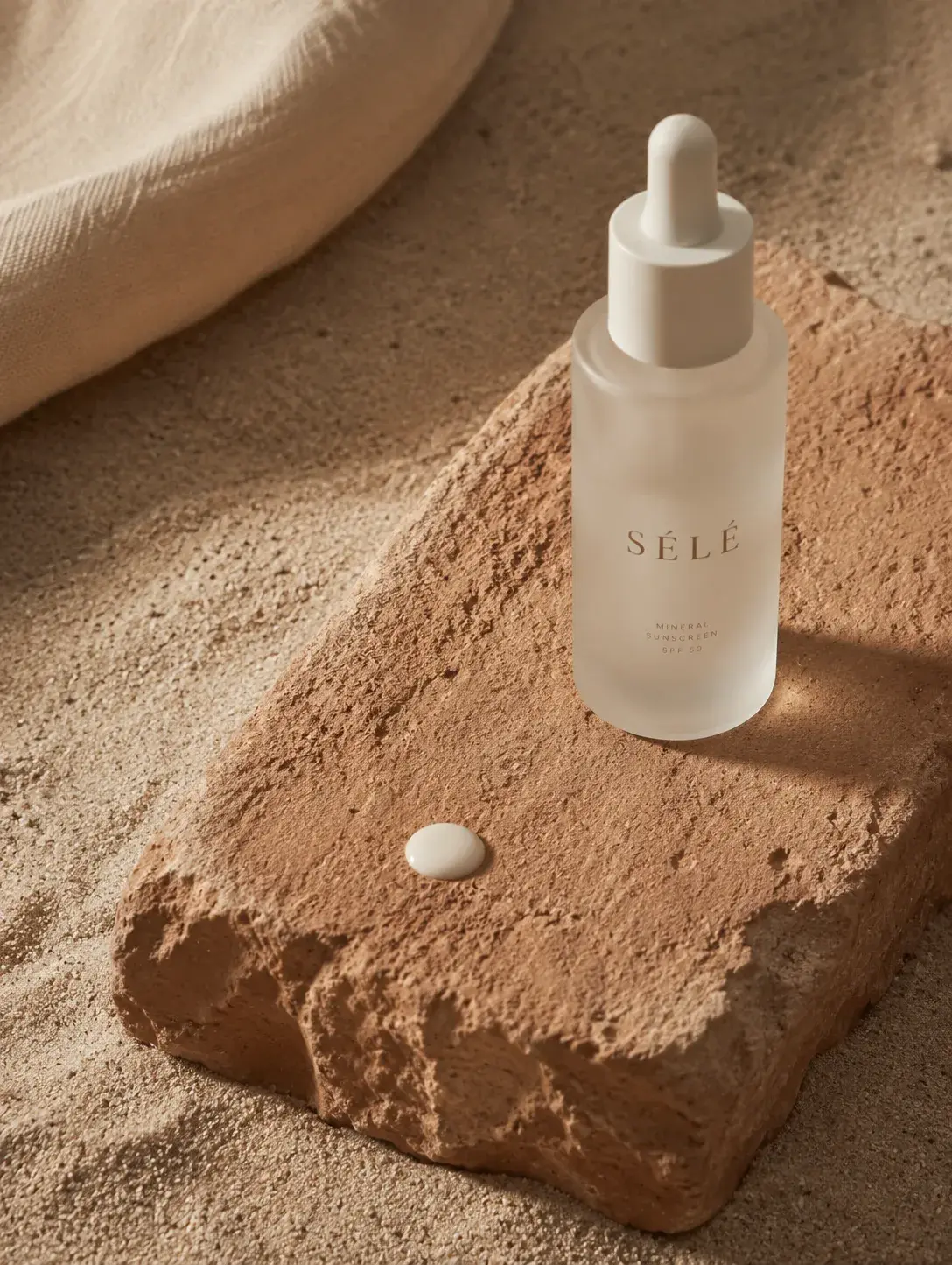 Flacon sérum pipette verre dépoli sur bloc de pierre – goutte de formule, sable, tissu blanc