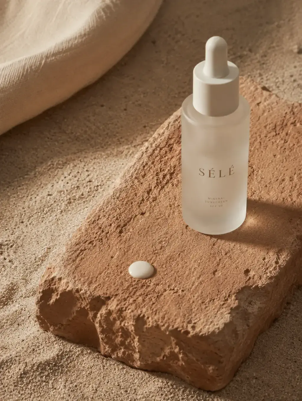 Flacon sérum pipette verre dépoli sur bloc de pierre – goutte de formule, sable, tissu blanc