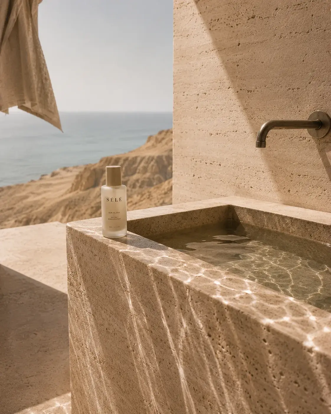 Flacon sérum sur bord de baignoire travertin extérieure – vue falaises et mer, robinet, salle de bain luxe