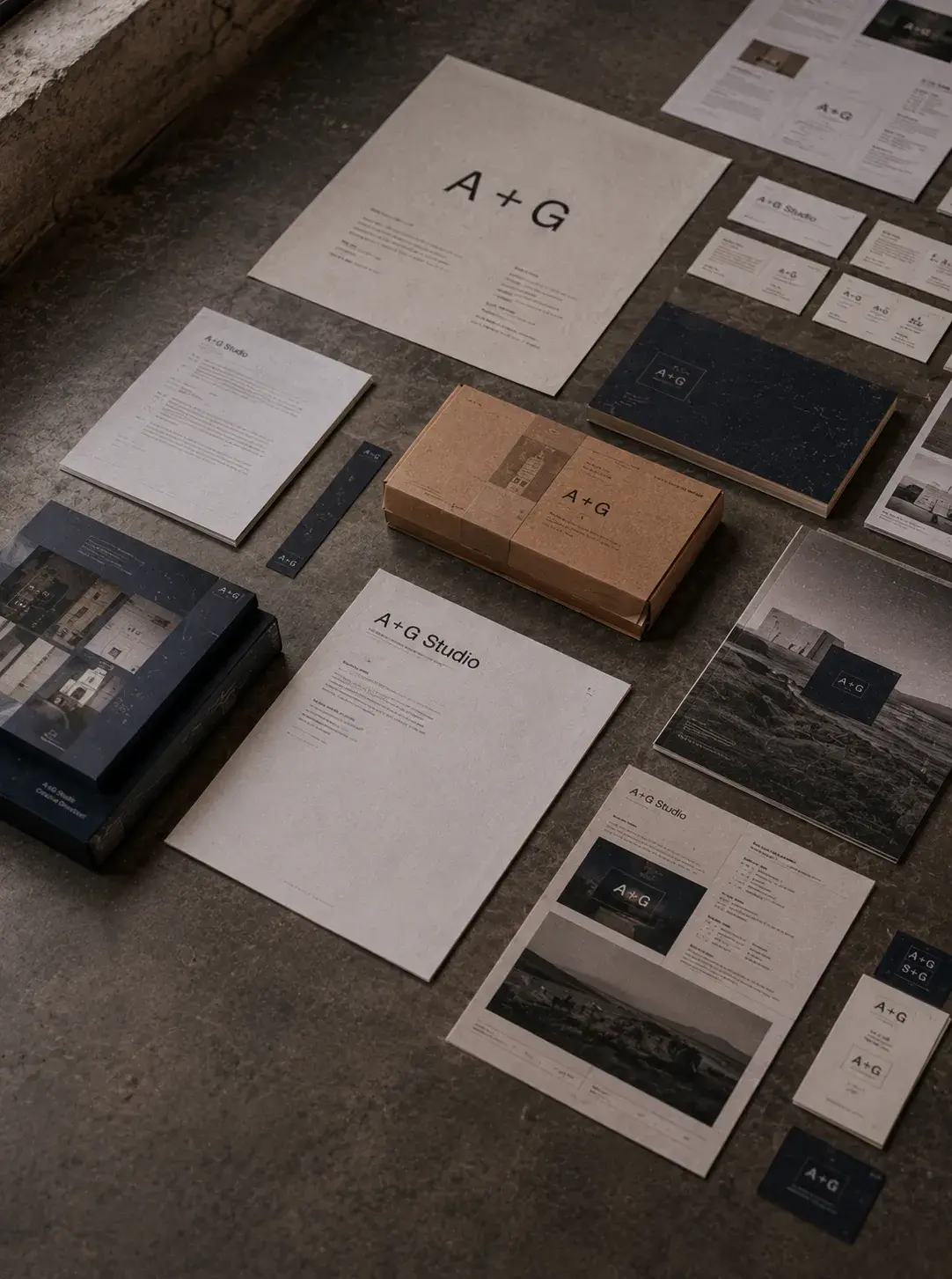 Flat lay sur sol béton de l'ensemble complet de l'identité visuelle A+G Studio — chartes, brochures, boîte kraft, cartes de visite