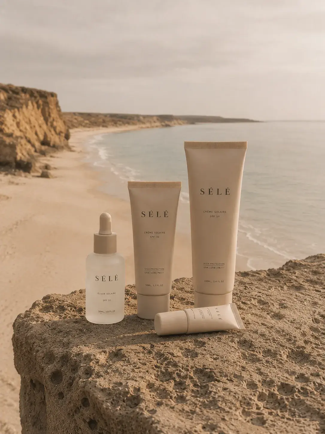 Gamme de soins solaires sur rocher côtier – mer grise, falaises, ciel nuageux, packaging beige