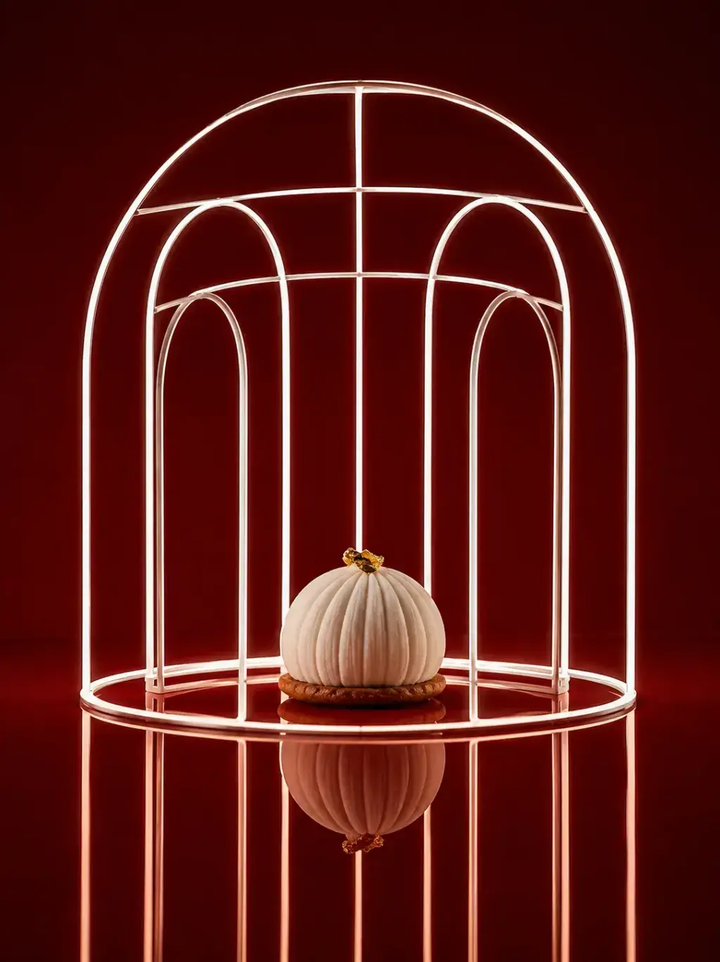 Gâteau citrouille côtelée blanche sur socle doré sous cage architecturale en fils dorés, table-miroir rouge avec reflet