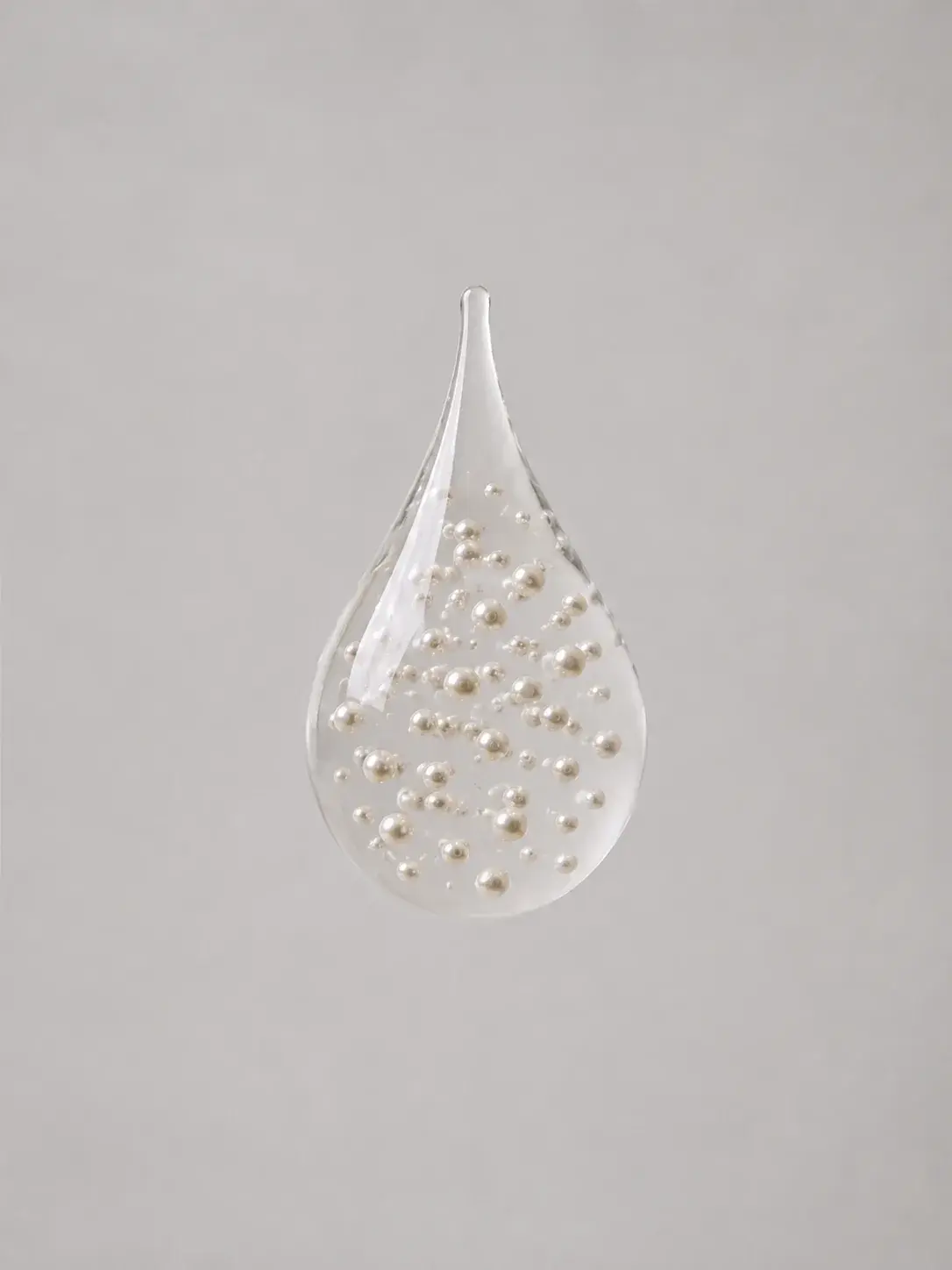 Goutte de verre transparente flottante renfermant des perles éparses en suspension, larme cristalline