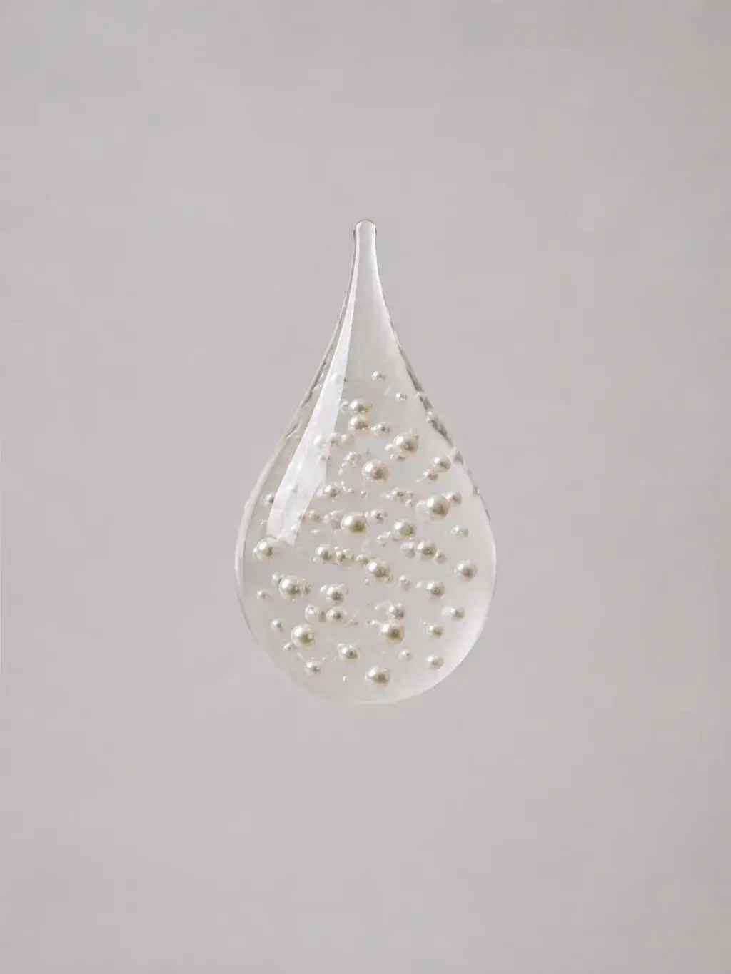 Goutte de verre transparente flottante renfermant des perles éparses en suspension, larme cristalline